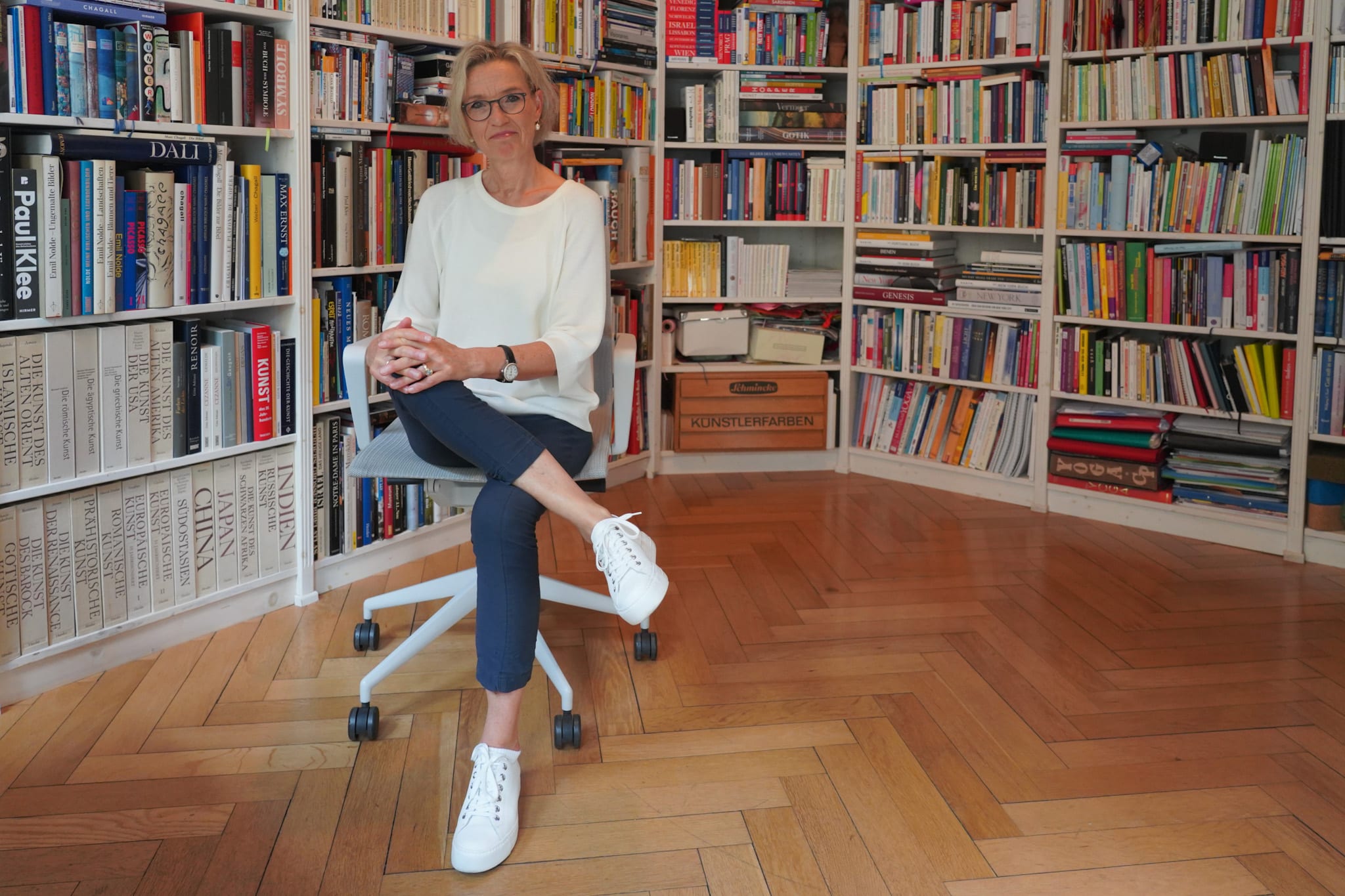 Claudia Peters sitzt auf einem Stuhl in ihrem Arbeitszimmer, ringsum deckenhohe Bücherregale.