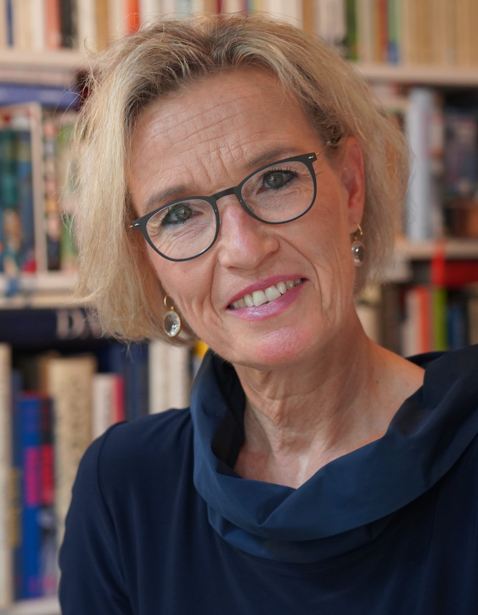 Claudia Peters im Portrait, lächelnd vor ihrem Bücherregal.